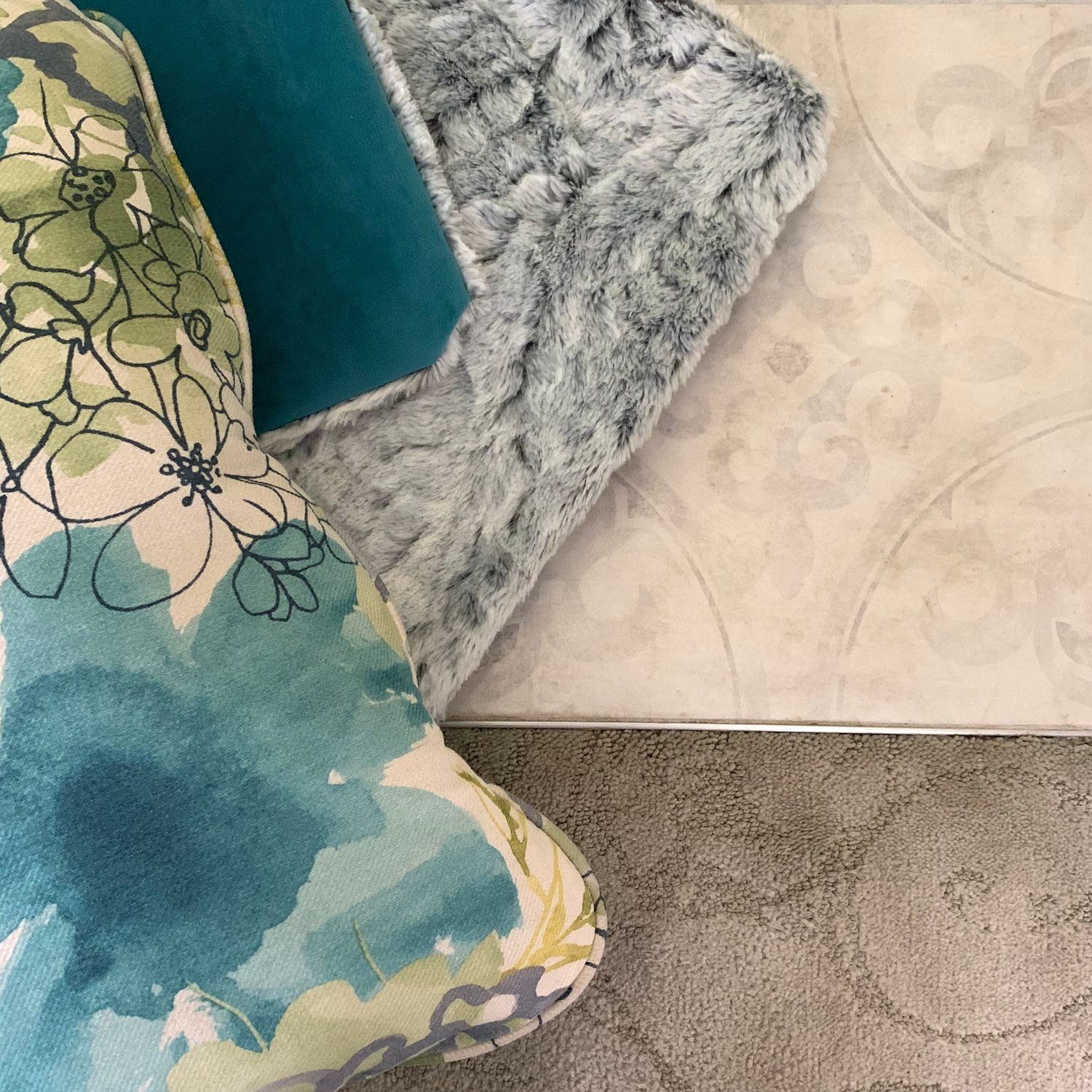 A pillow with flowers on it sits on a carpet next to a blanket