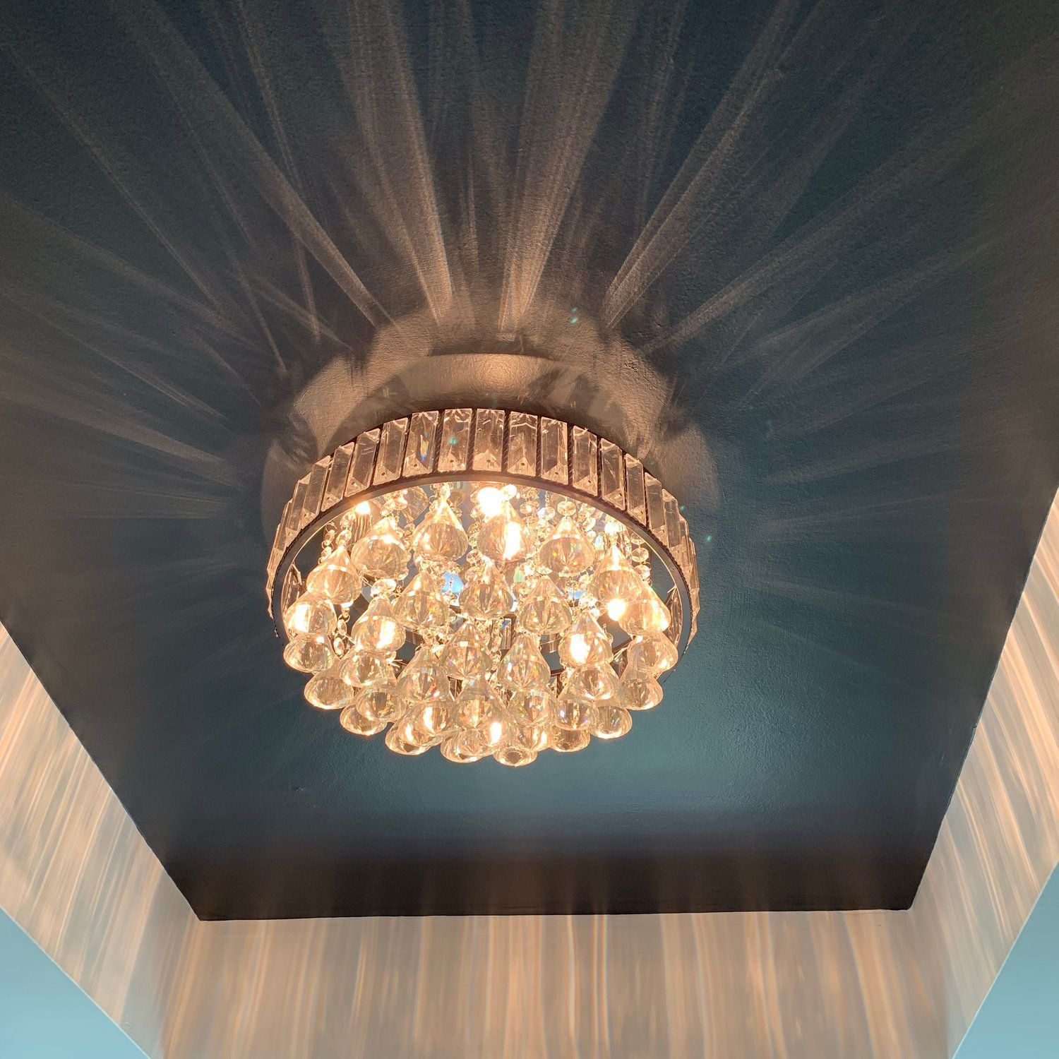 A crystal flush-mount chandelier casts light patterns onto a dark blue ceiling.
