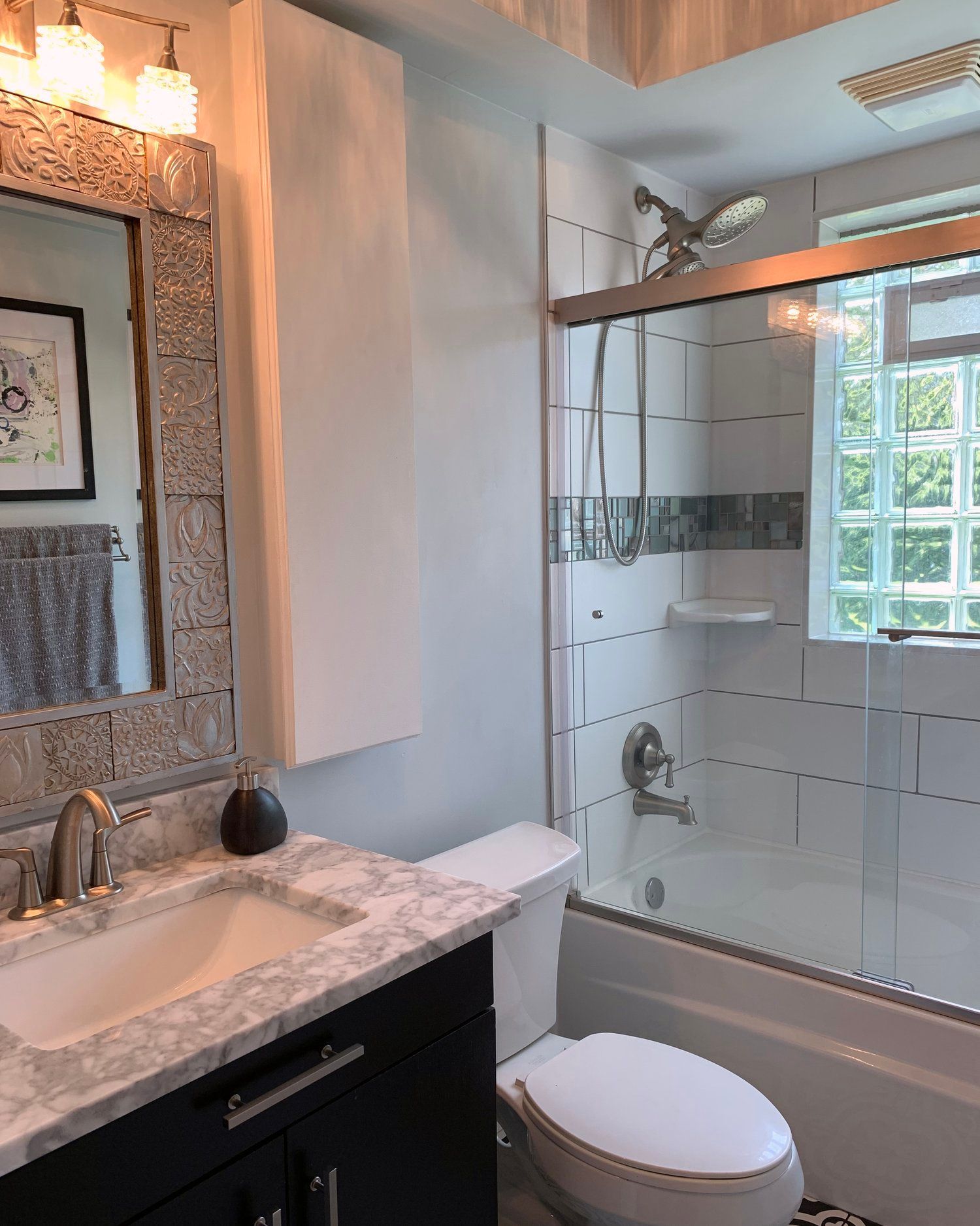 A bathroom featuring a dark vanity with a white marble countertop, a decorative framed mirror, and a tiled shower-tub.