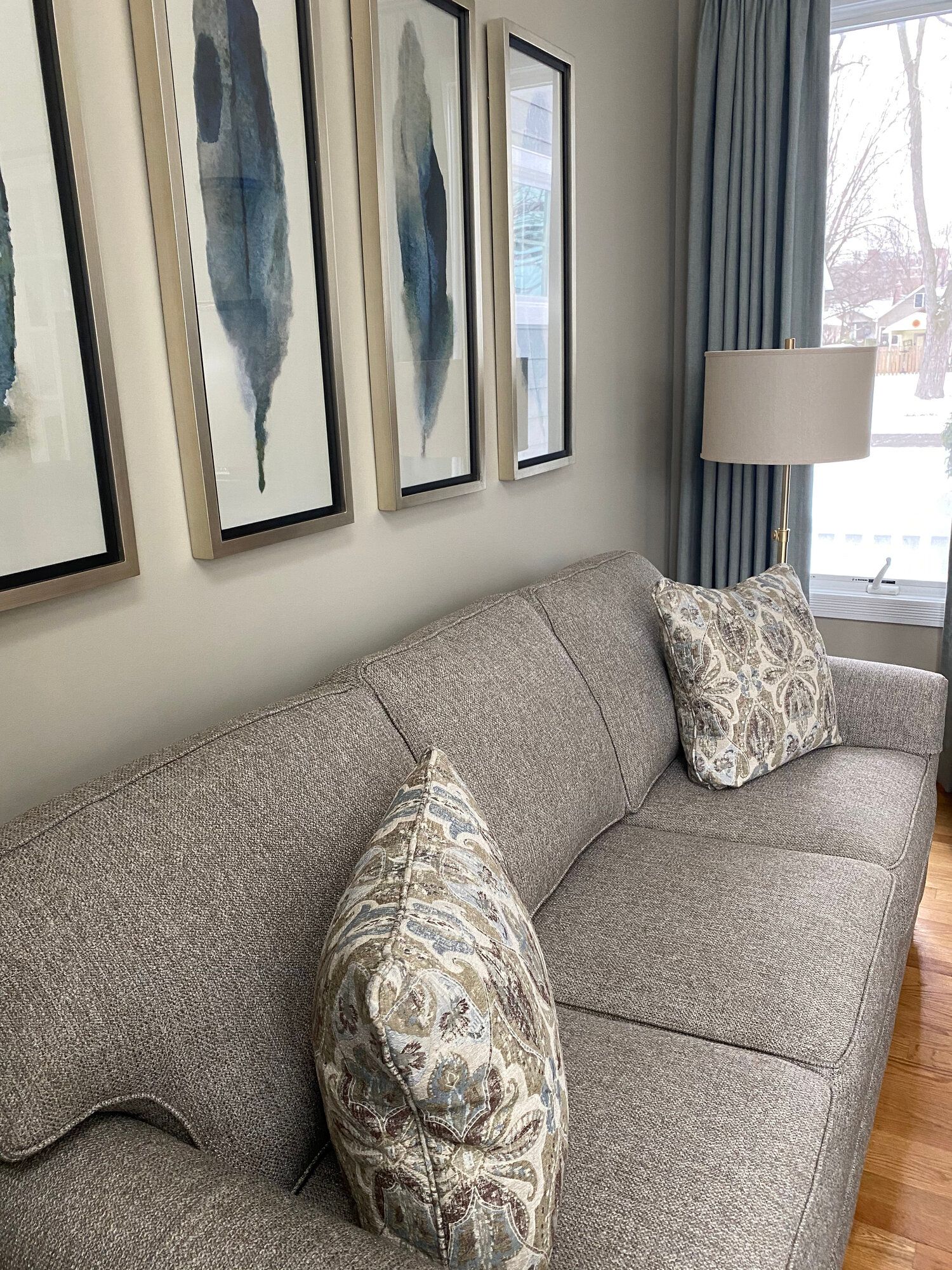 A living room with a couch , lamp , and paintings on the wall.