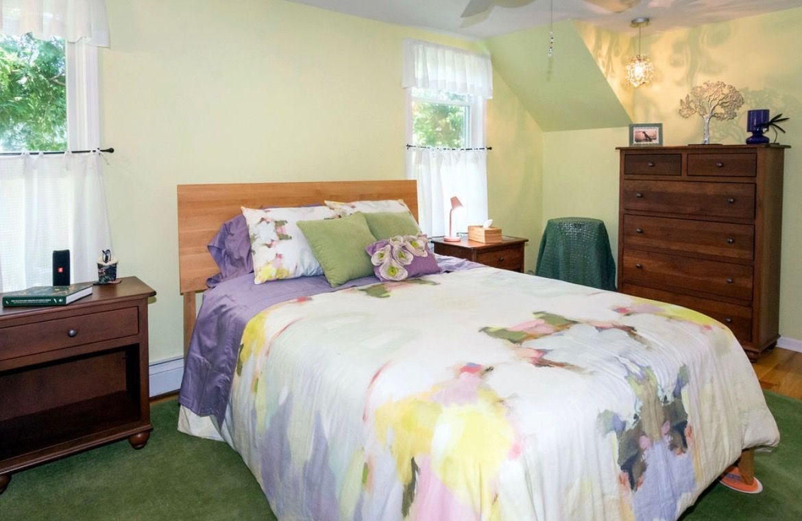 A bedroom with light green walls, a bed featuring a floral comforter, a wood dresser, and matching nightstand.