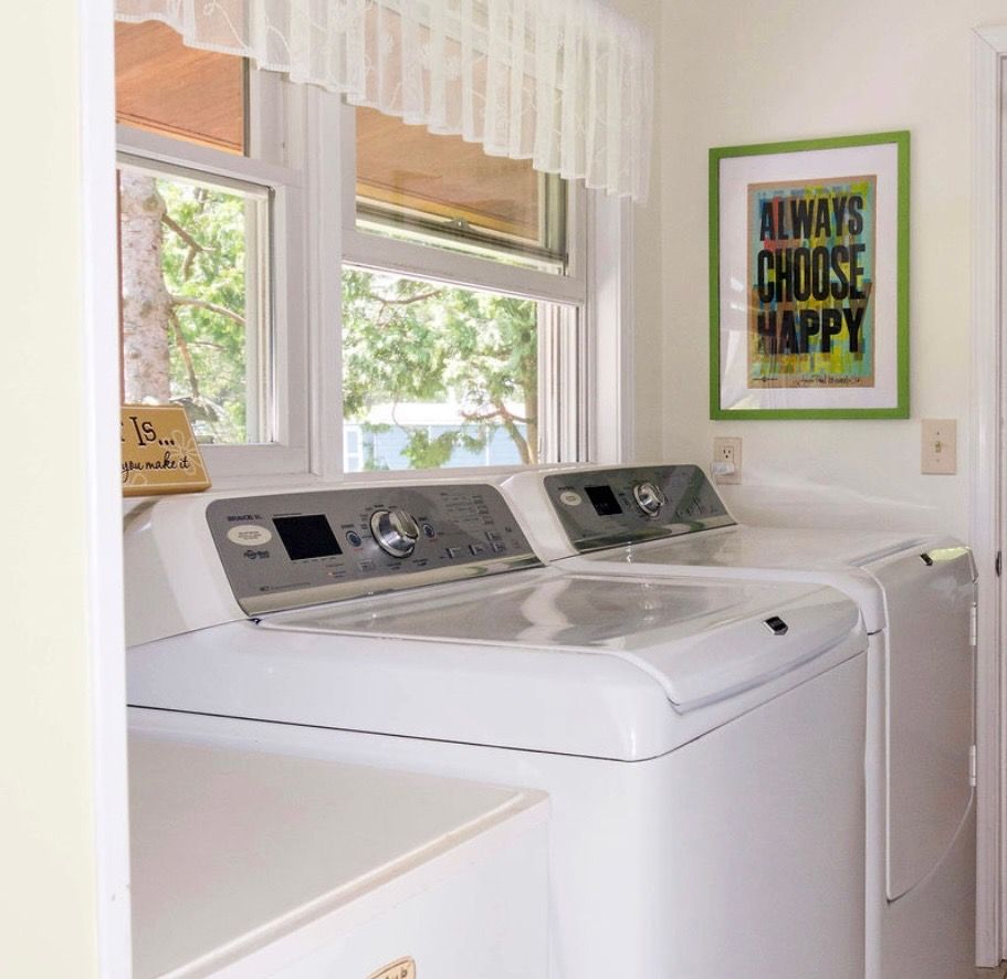 A laundry room featuring two white washing machines near a window with a green-framed 
