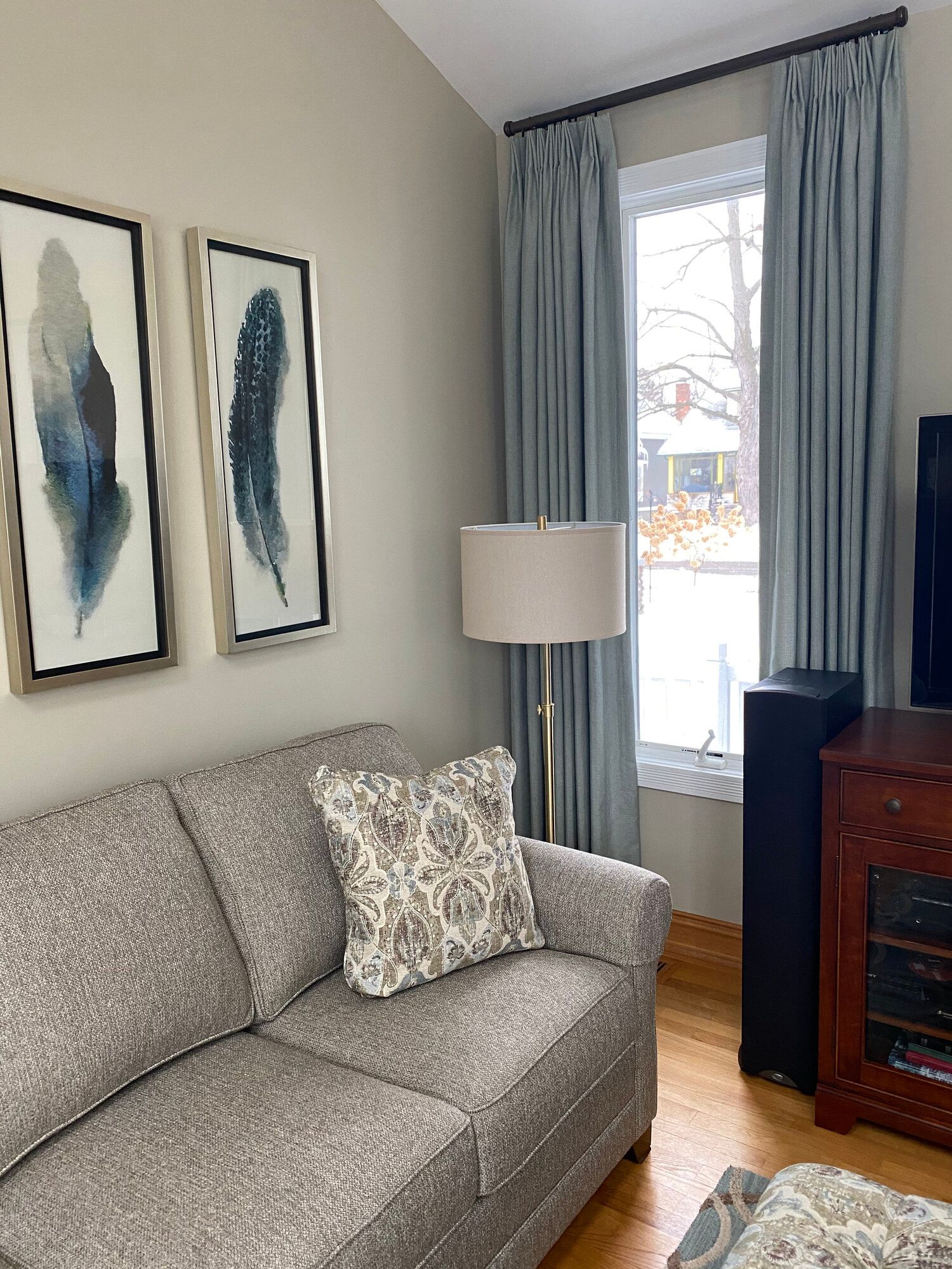 A living room with a couch , ottoman , lamp , and two paintings on the wall.