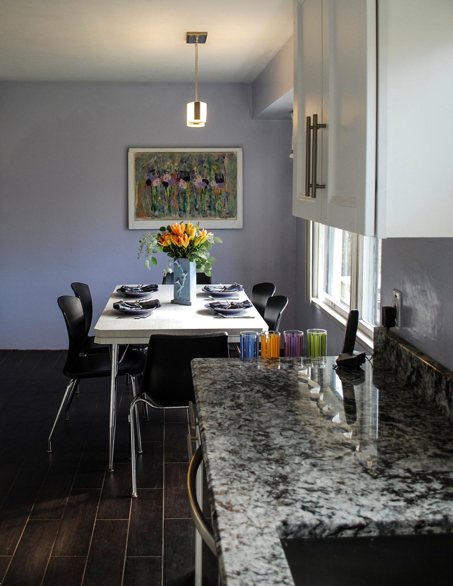 A dining area with a white table and black chairs, adjacent to a kitchen counter with granite surfaces and white cabinets.