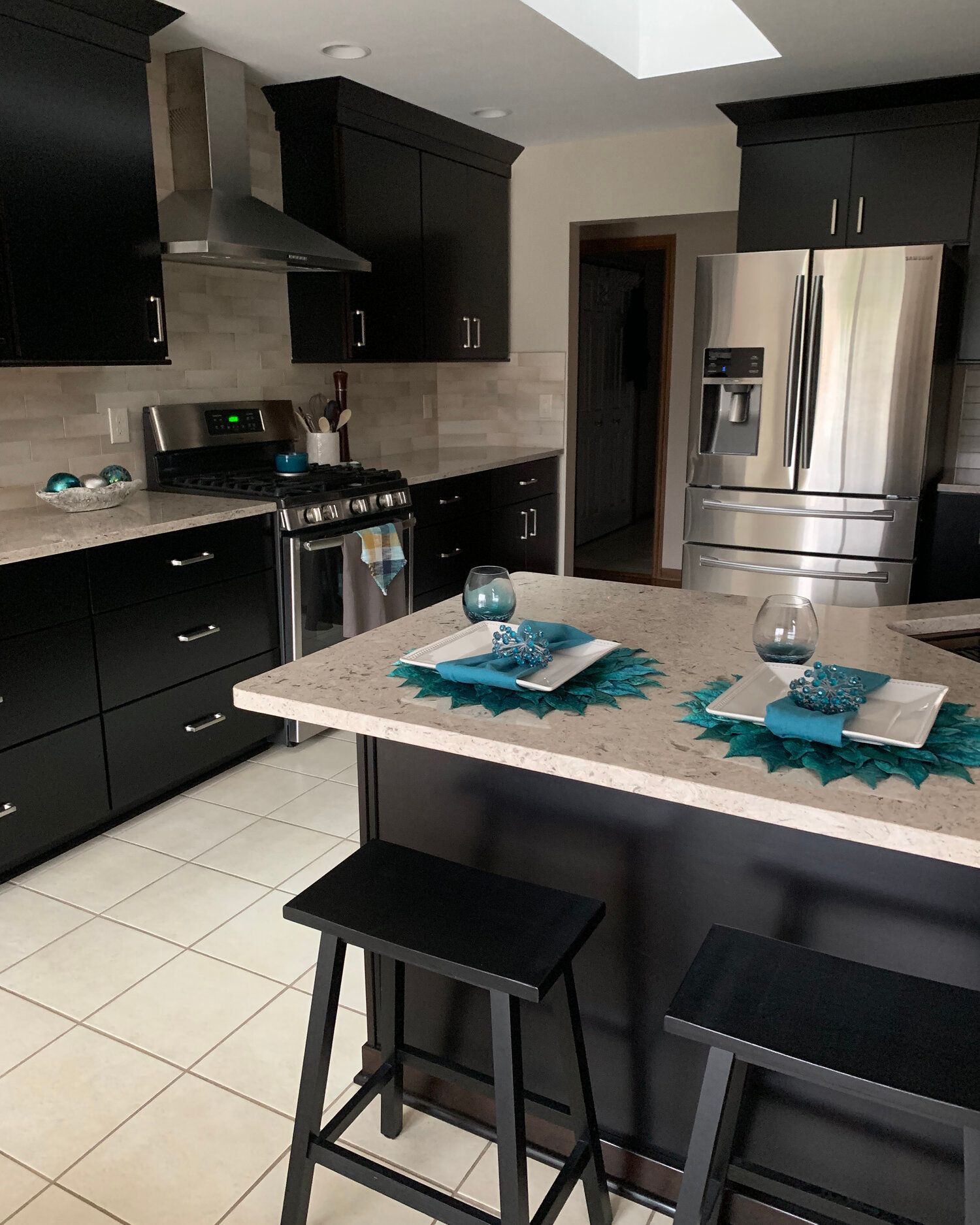 A kitchen with black cabinets and a stainless steel refrigerator