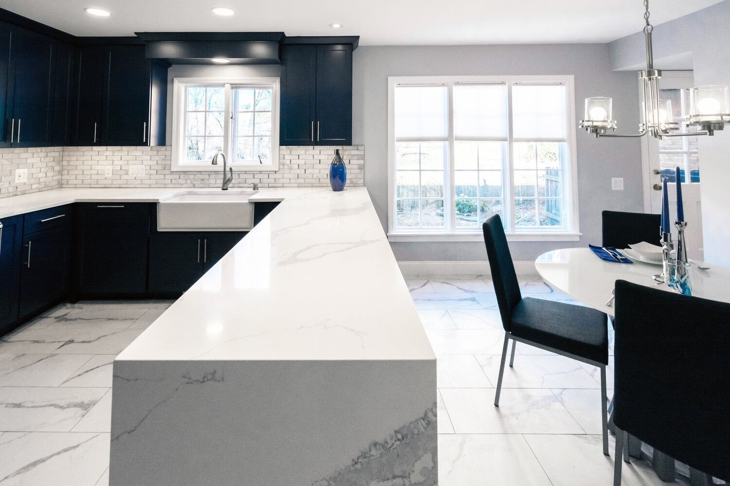 A kitchen with blue cabinets and white counter tops and a dining room with a table and chairs.