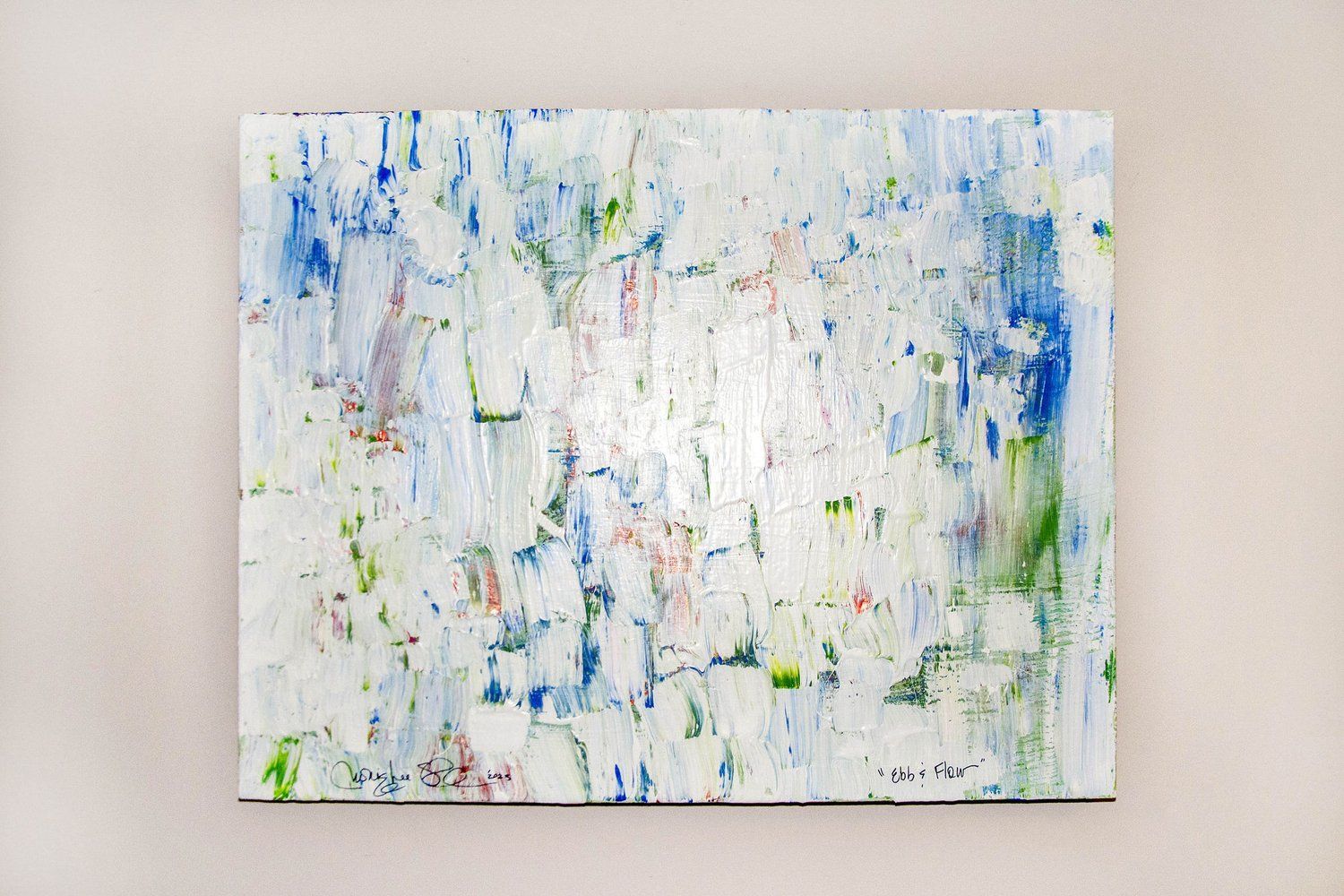 A large colorful painting is hanging on a white wall.