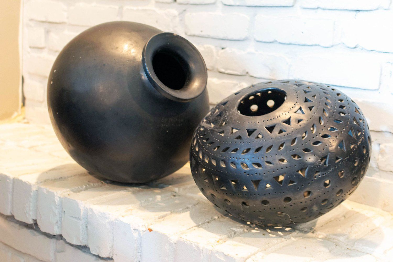Two black vases are sitting on a white brick fireplace mantel.
