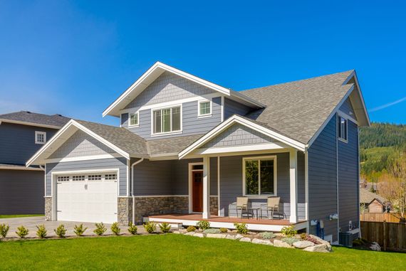 Two-story gray house with white trim, front porch, and garage under a blue sky