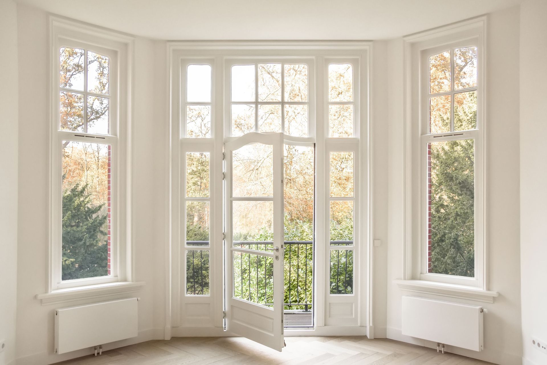 Bright bay window and glass door in a white room, opening to an outdoor balcony.