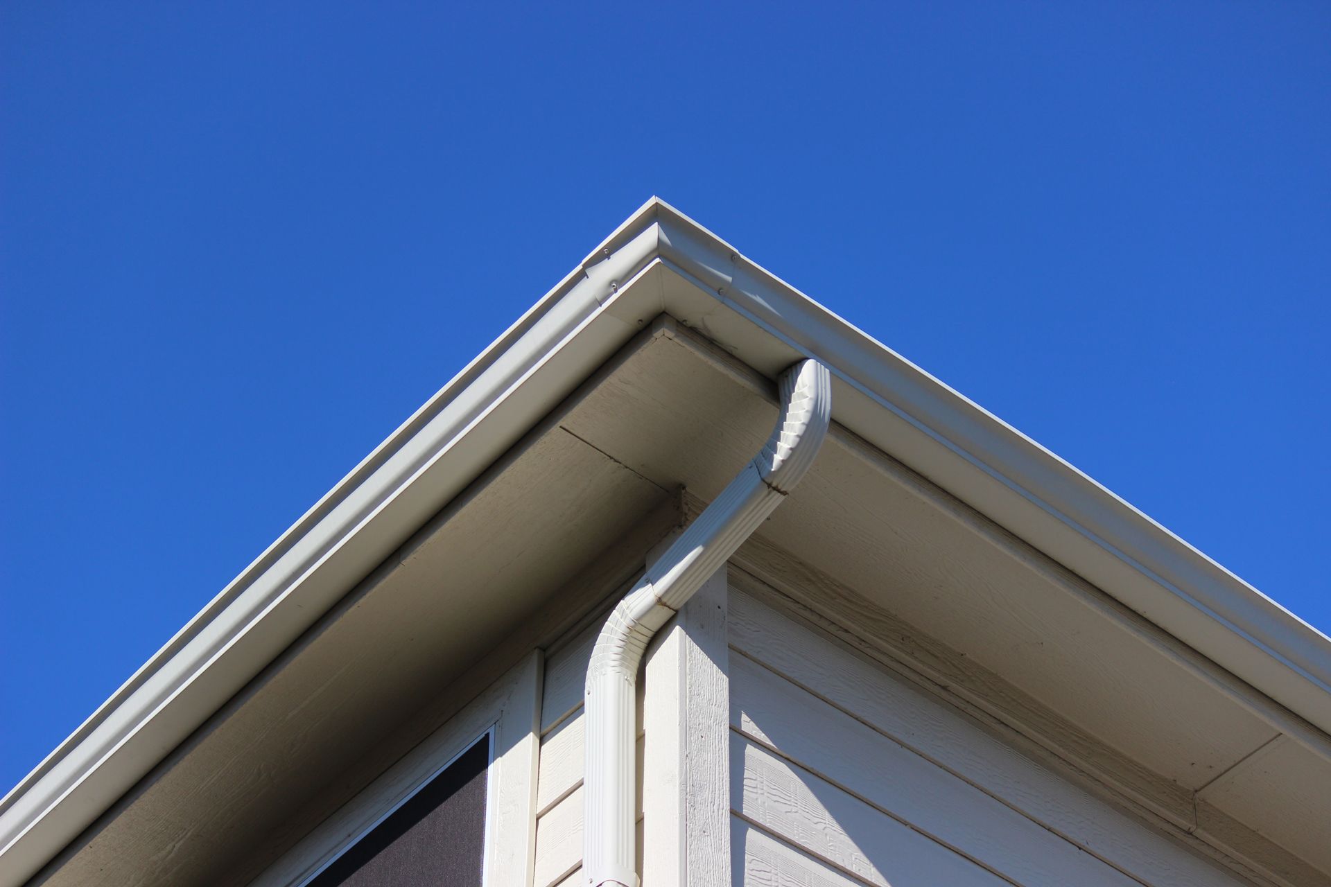 Corner of a house roof with white gutters against a clear blue sky