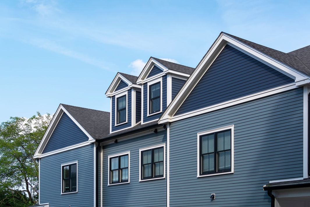 Blue-gray house exterior with dormer windows and white trim under a clear sky