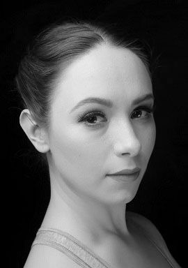 Woman with hair up, looking slightly to the side, wearing a top, against a black background.