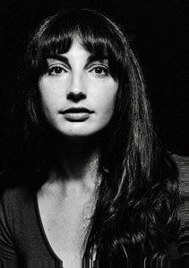 Woman with long dark hair, bangs, gazing forward; black and white portrait.