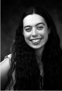 Woman with long, wavy hair smiles broadly, facing forward. B&W portrait with dark background.