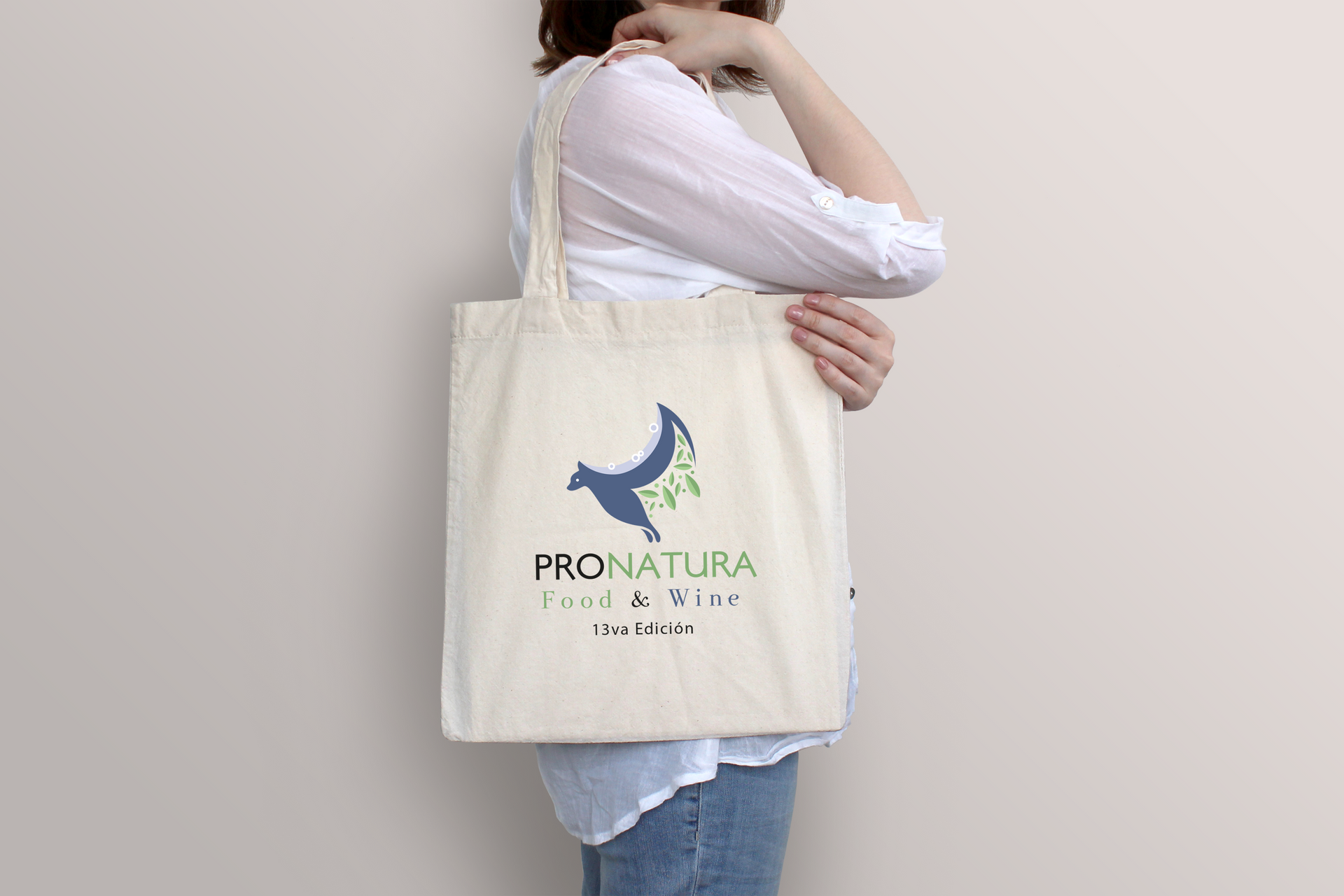 Una persona lleva una bolsa de lona de color claro con el logotipo de ProNatura sobre un fondo liso y claro.