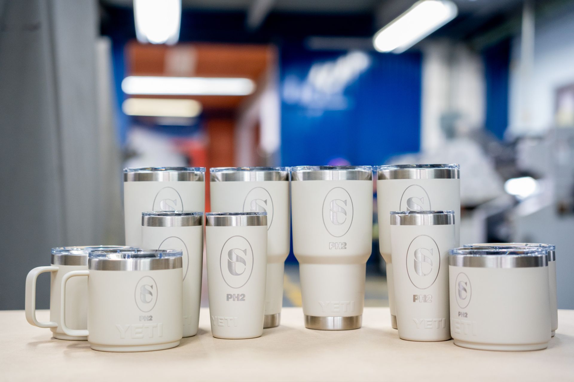 Una colección de vasos y copas aislantes de color crema con un logotipo en un entorno de fábrica.