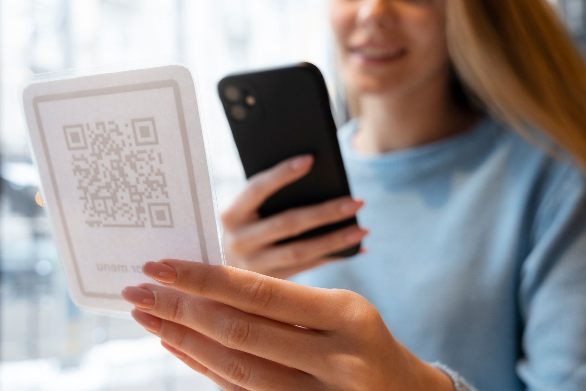 Una persona sostiene un teléfono para escanear una tarjeta blanca que contiene un código QR, en un entorno interior luminoso.