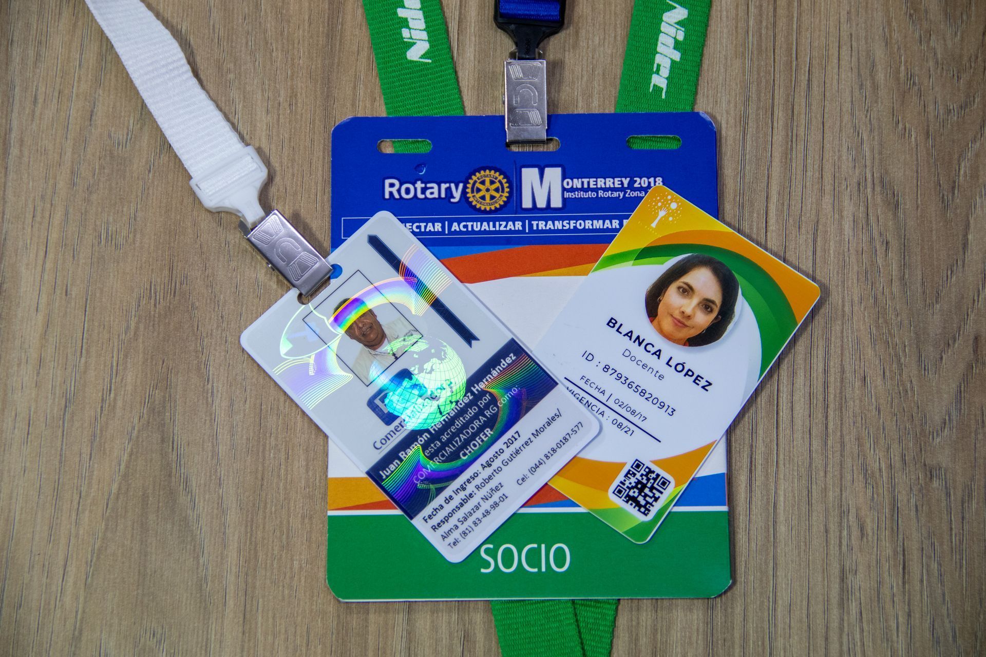 tarjetas de identificación del club rotario con fotografías, nombres y un código QR en una superficie de madera.