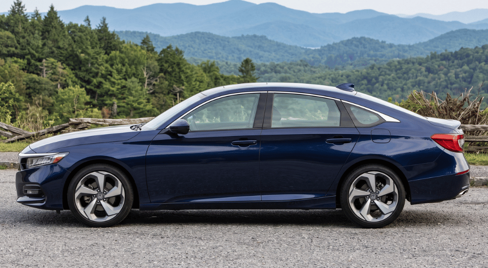 Dark blue sedan parked on a gravel overlook with forested mountains in the background