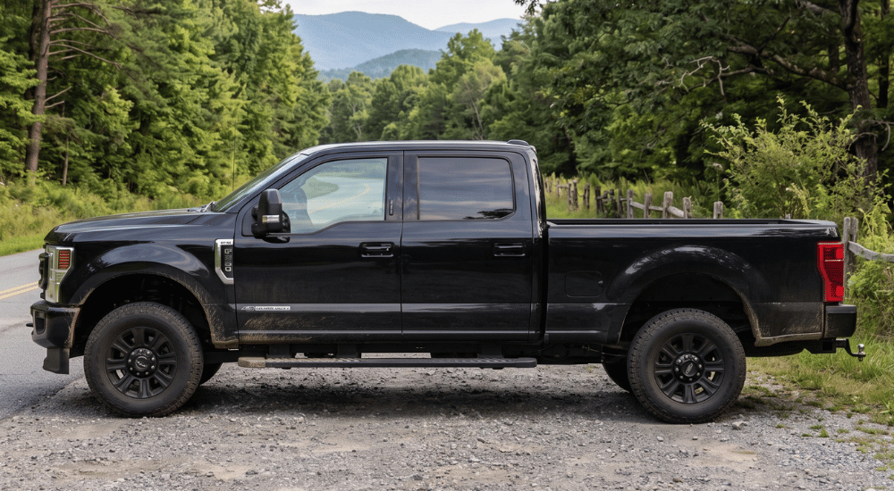 Black pickup truck parked on a gravel road with forested mountains in the background
