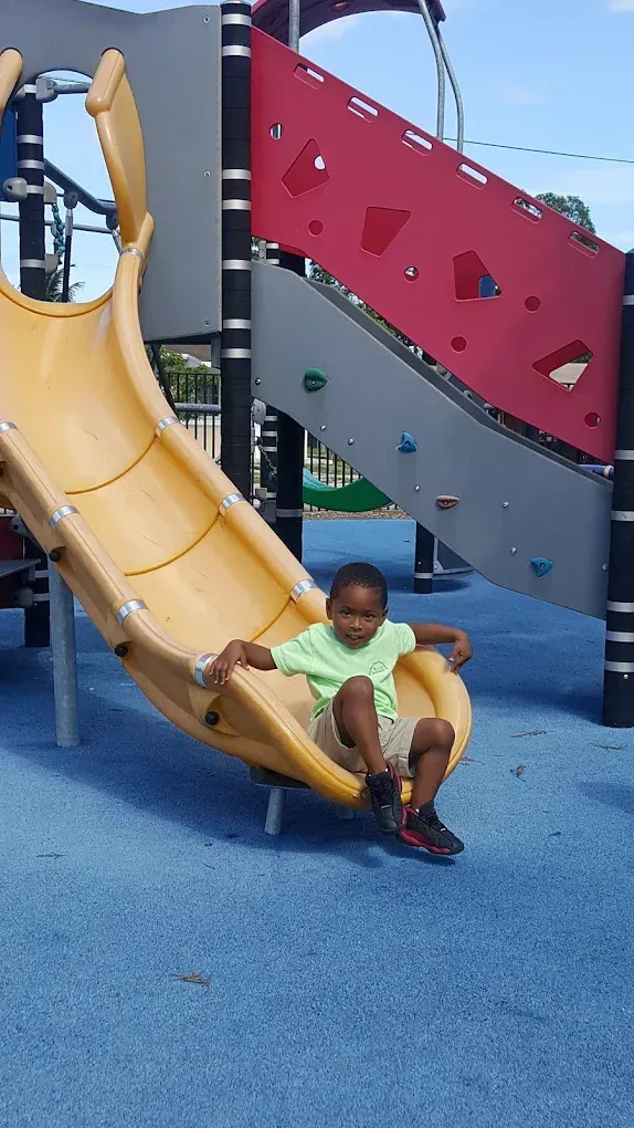 A child in a light green shirt sitting at the bottom of a curved yellow playground slide.