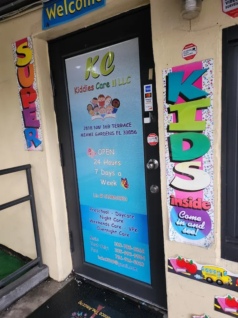 The entrance to a daycare facility with a glass door displaying contact details, hours, and colorful signs for kids.