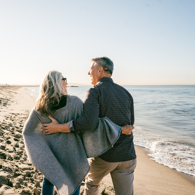 A man and a woman are standing on a beach looking at the ocean.