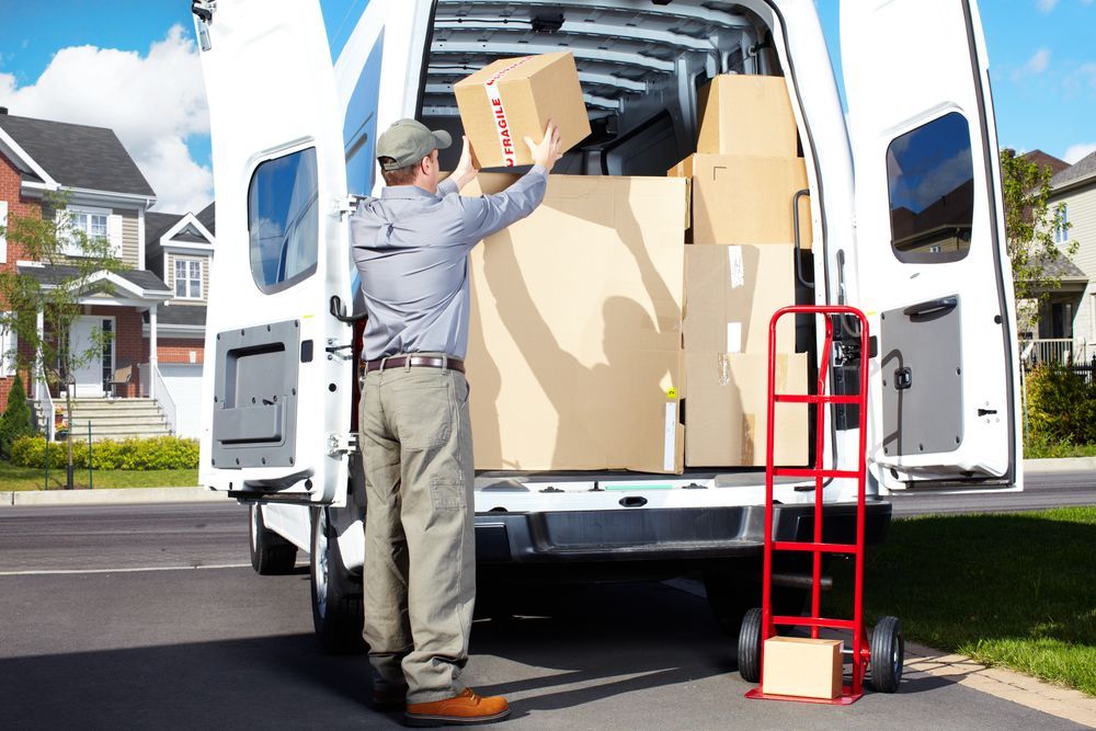 Two Movers Lift a Wrapped Sofa in a Room With Boxes and Furniture — Uplift Removals in Gold Coast, QLD