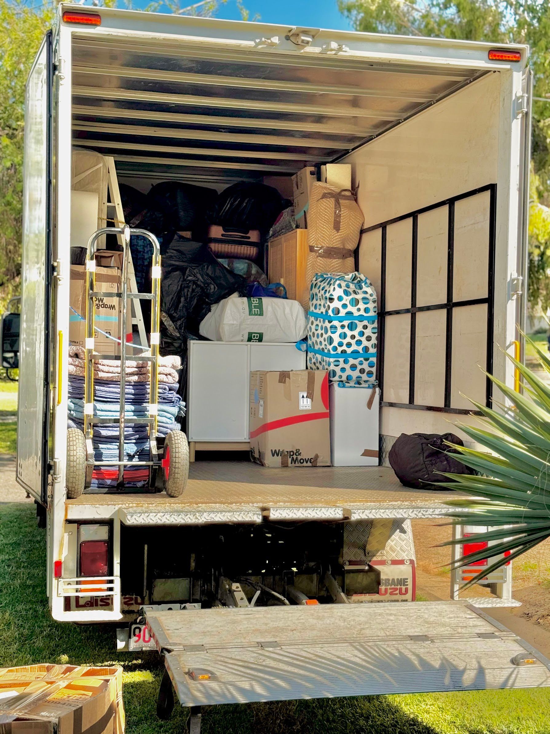 Two Movers in Blue Cover a Wrapped Cabinet With Padding in a White Room — Uplift Removals in Brisbane, QLD