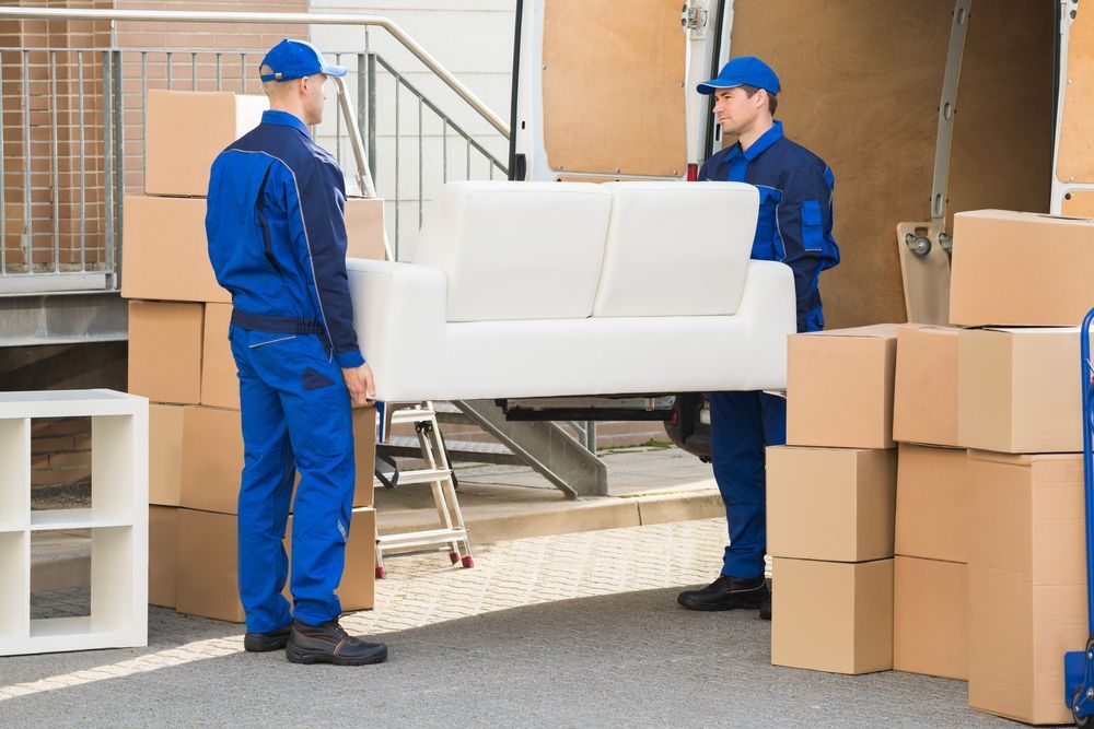 Two Movers in Blue Uniforms Carrying a White Sofa Towards a Truck — Uplift Removals in Marsden, QLD
