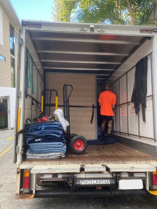 A Man Is Standing In The Back Of A Moving Truck — Uplift Removals in Burdell, QLD