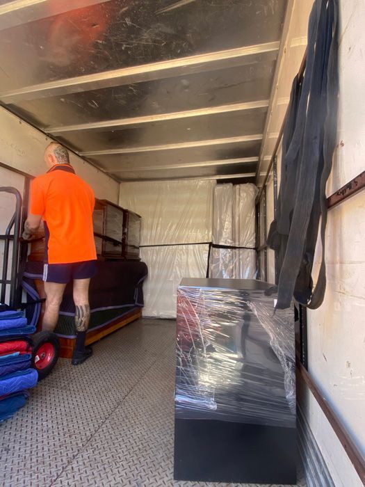 A Man Is Pushing A Piano Into A Moving Truck — Uplift Removals in Burdell, QLD