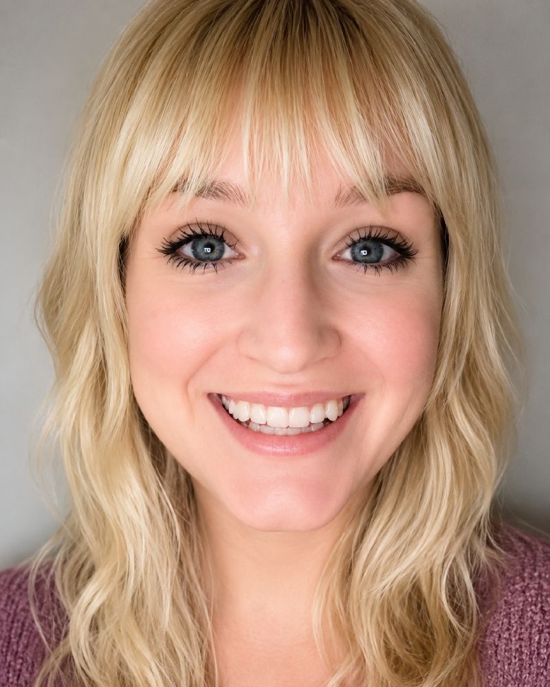 Smiling blonde woman with bangs in a pink sweater against a gray background