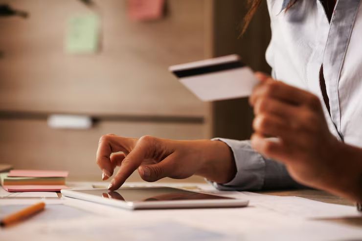 Hands writing on paper at a desk with a credit card nearby, in a softly lit office setting