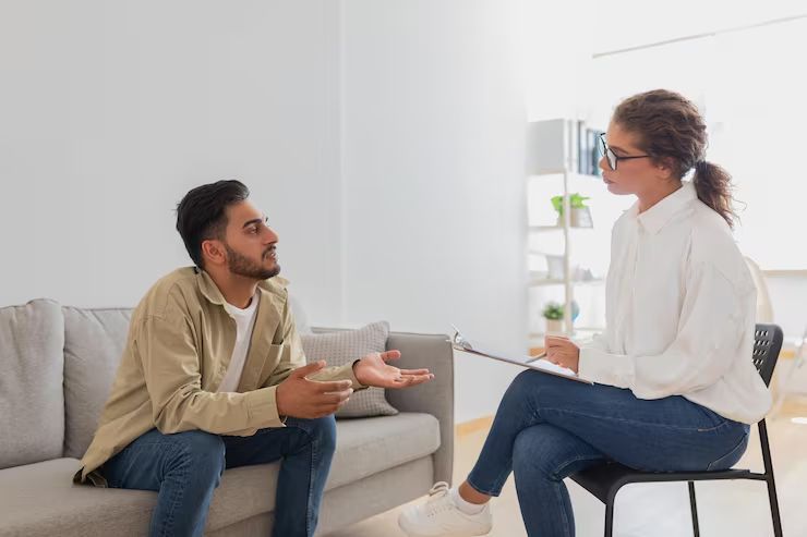 Two people talking in a bright living room, seated on a sofa and chair during a 상담 session.