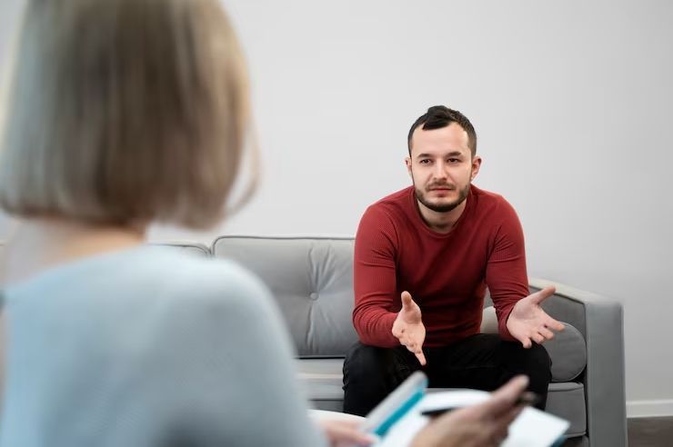 Man in red sweater talking on a gray couch during a counseling session