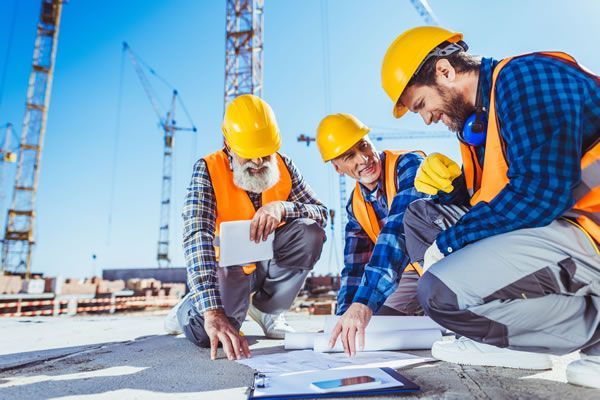 Um grupo de trabalhadores da construção civil está olhando para uma planta de um canteiro de obras.