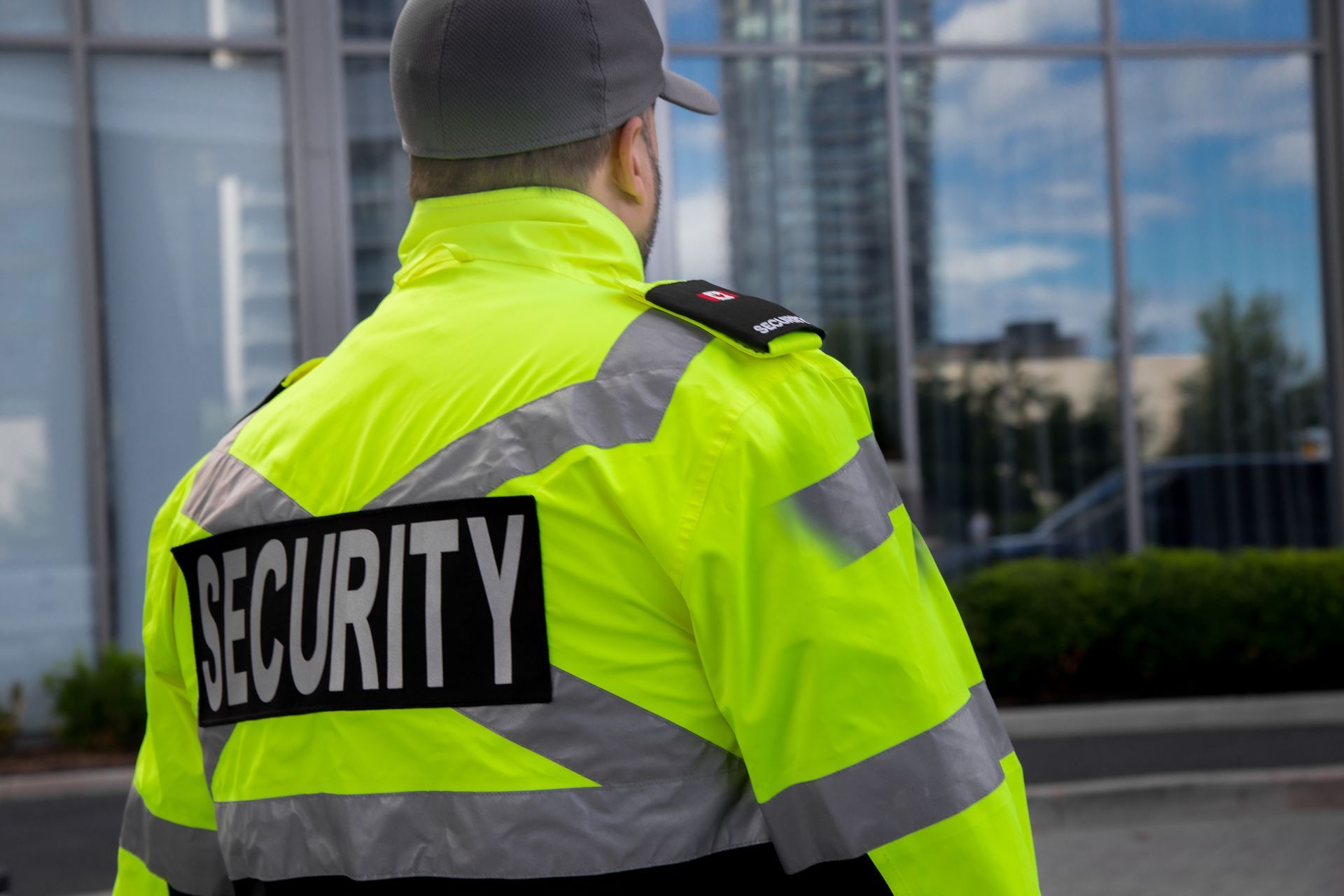 Security guard in a neon yellow jacket standing outside a glass building.