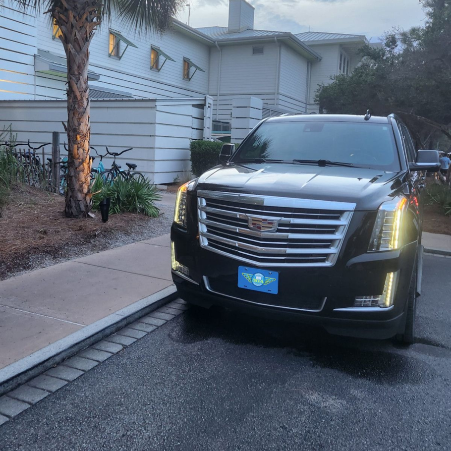 Black Cadillac Escalade parked in front of a white building with palm trees.