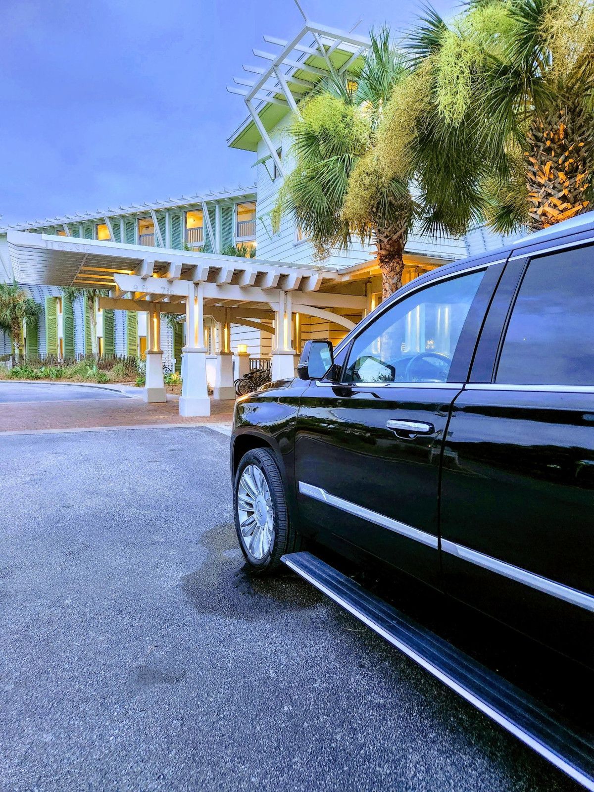 Black SUV parked in front of a light green building with a white pergola and palm trees.