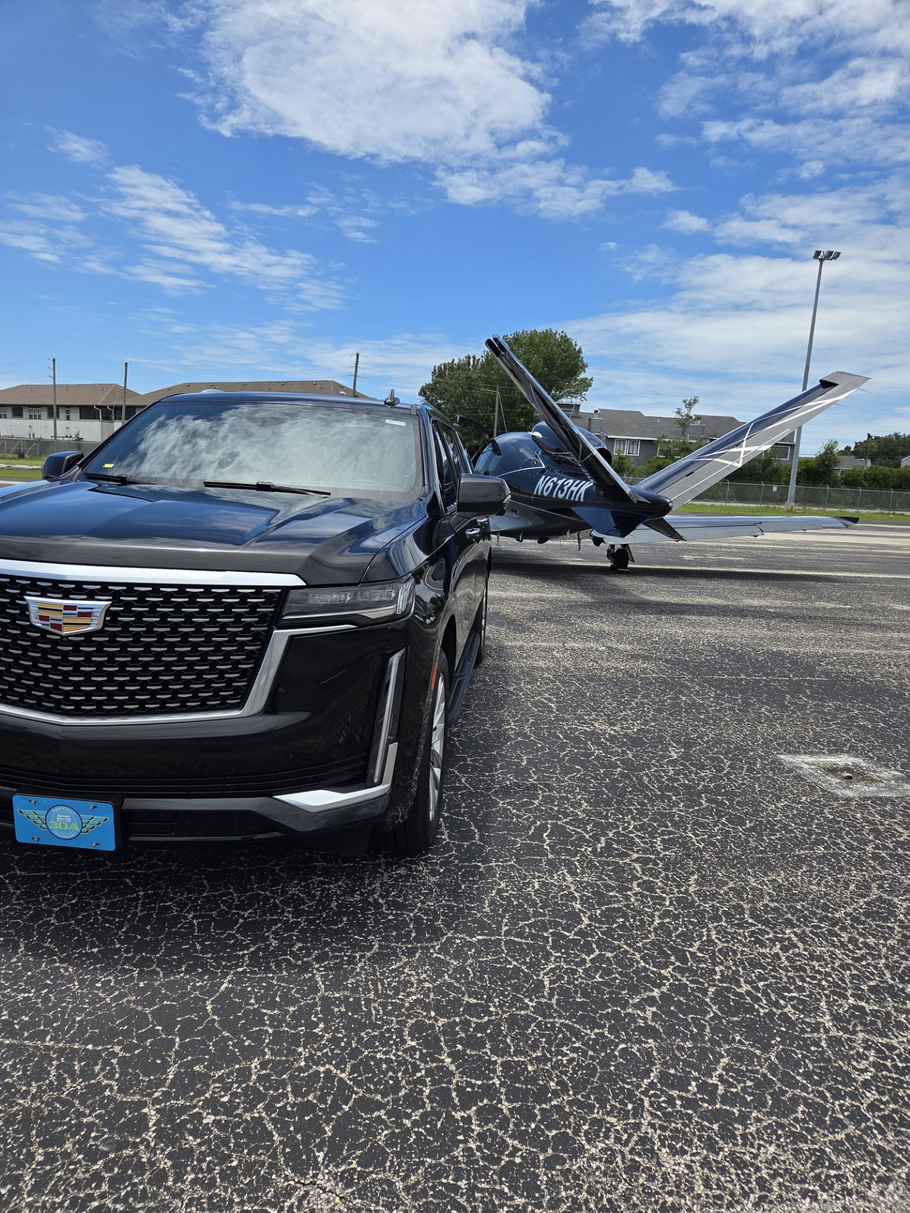 Black Cadillac SUV parked in front of a white building with a palm tree, bikes, and overcast sky.