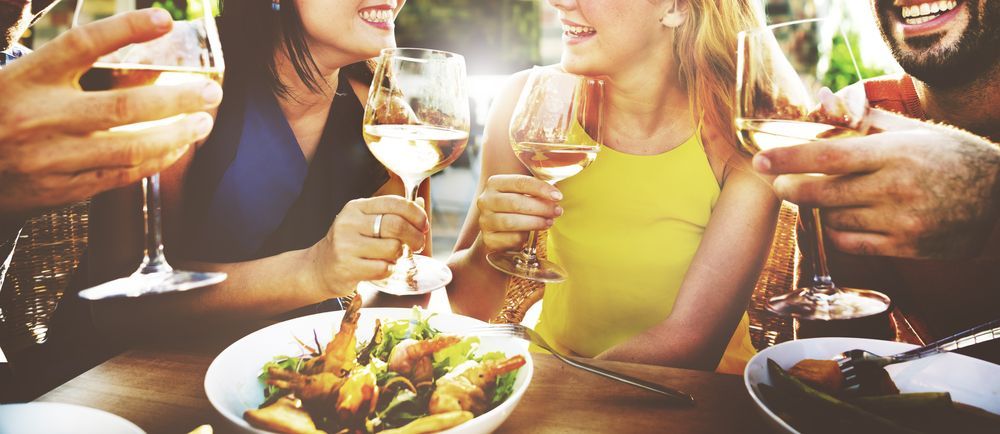 A group of people are sitting at a table eating food and drinking wine.