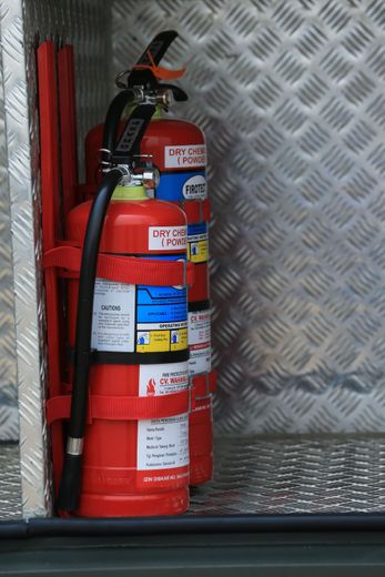 Red fire extinguisher secured in a vehicle compartment with a diamond-plate metal wall background