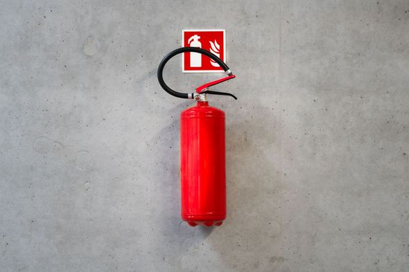 Red fire extinguisher mounted on a gray concrete wall beneath a fire safety sign
