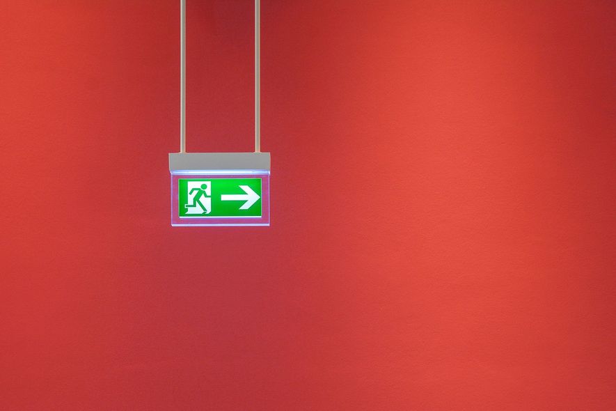 Green emergency exit sign with a right arrow hanging against a red wall