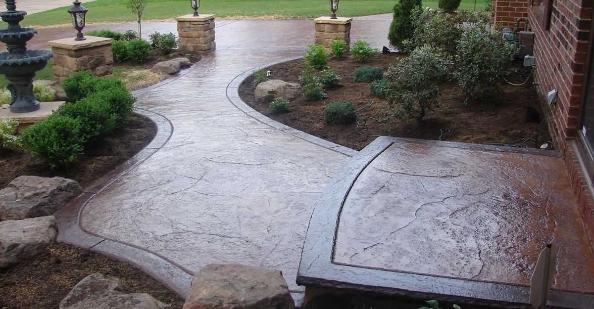 Wet stone walkway curving through a landscaped front garden beside a brick house