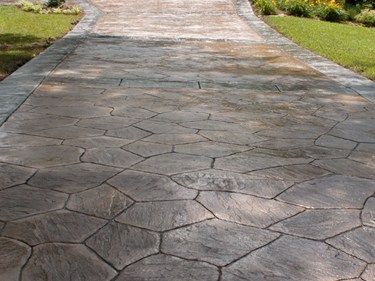 Cracked stamped-concrete driveway bordered by green grass and shrubs