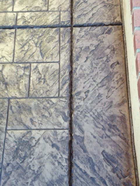 Stamped concrete walkway with a narrow crack along the center, bordered by brick.