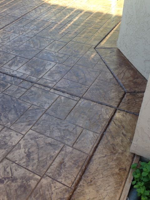 Stamped concrete patio beside a house wall, with sunlight and a small green plant in the corner